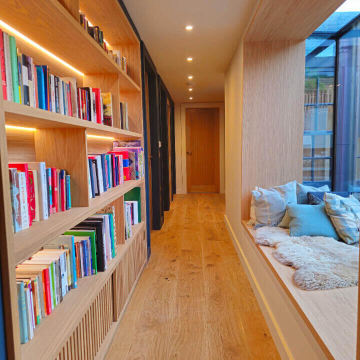 Bespoke Built-In Oak Bookcase and Custom Window Seat Joinery Bespoke built-in hallway oak bookcase with integrated back lighting opposite a fitted oak window seat which is crafted from hand-selected solid oak and veneer. made by Fundi Joinery in Edinburgh