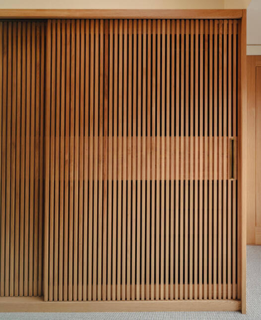 Large sliding slatted wardrobe doors made from hand-selected European oak and premium veneer with a naturally patinated brass pull handle. made by Fundi Joinery in Edinburgh, Scotland